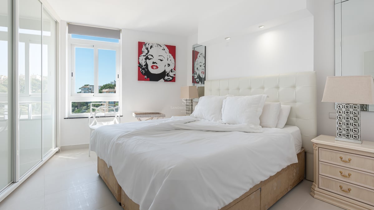 Chambre moderne avec tête de lit capitonnée blanche, grandes baies vitrées et art pop coloré.