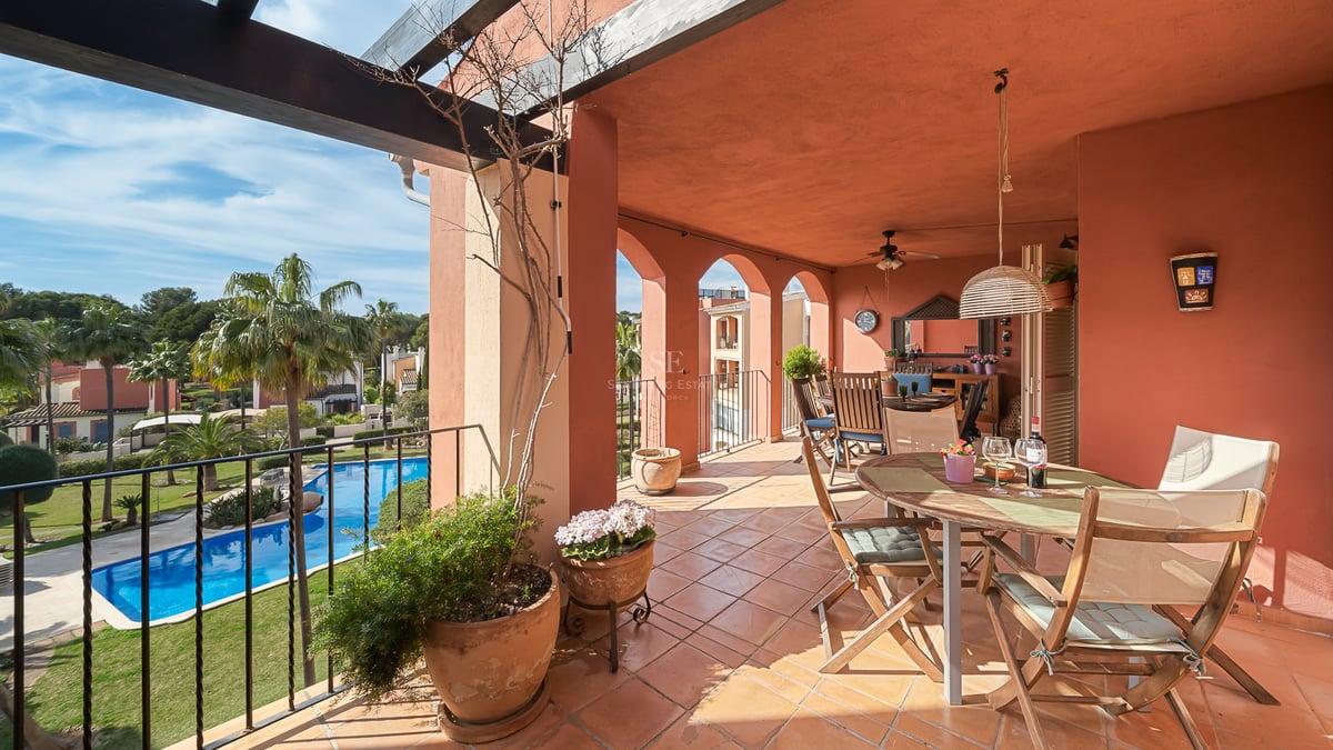 Terrasse en terre cuite avec mobilier de repas extérieur surplombant une piscine et des palmiers.