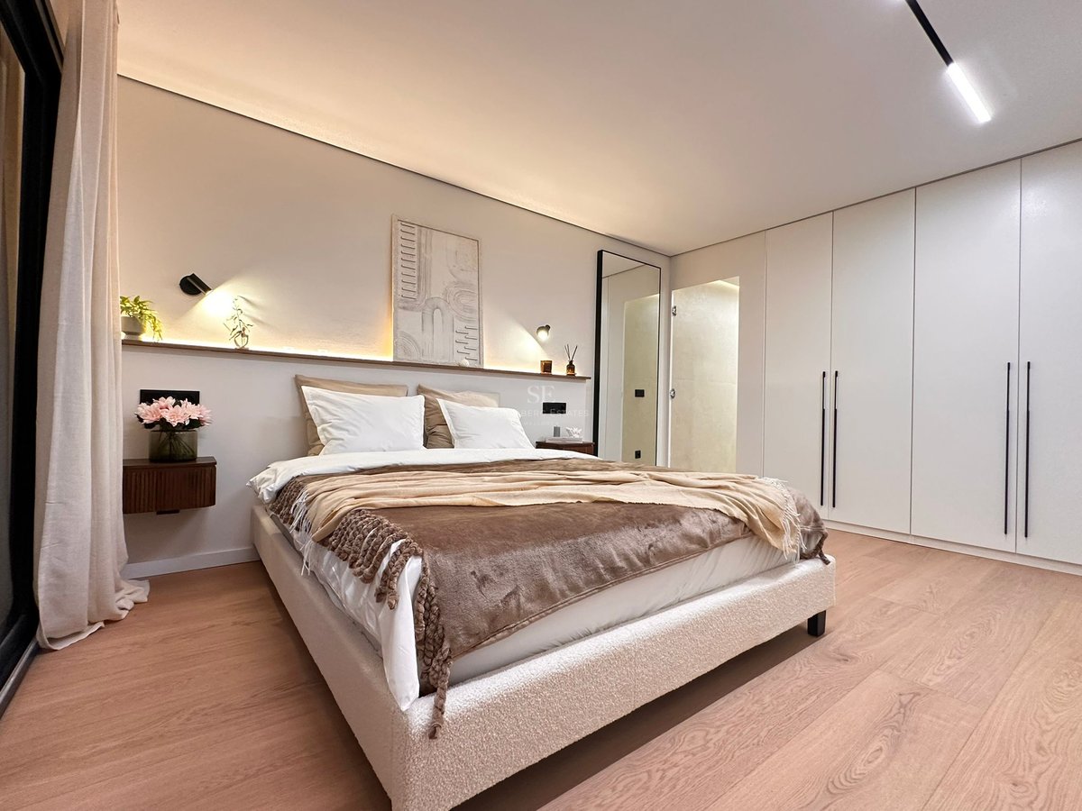 Chambre de maître moderne avec lit en bouclé, éclairage d'ambiance en tête de lit et parquet en bois clair.