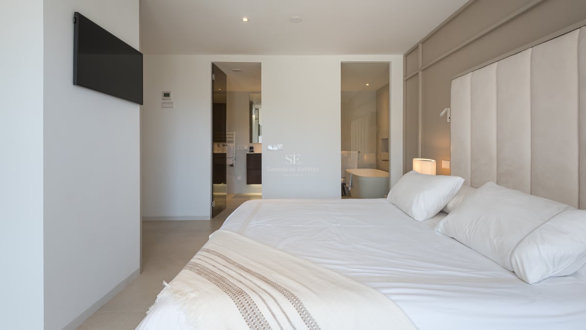Chambre de maître moderne avec grand lit, tête de lit rembourrée et vue sur la salle de bain privative.