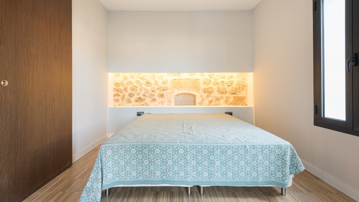 Chambre à coucher avec un lit, un mur en pierre éclairé par l'arrière et du parquet au sol.