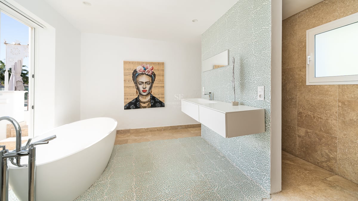 Salle de bain lumineuse avec baignoire ovale, lavabo suspendu, mur en mosaïque bleue et portrait de Frida Kahlo.