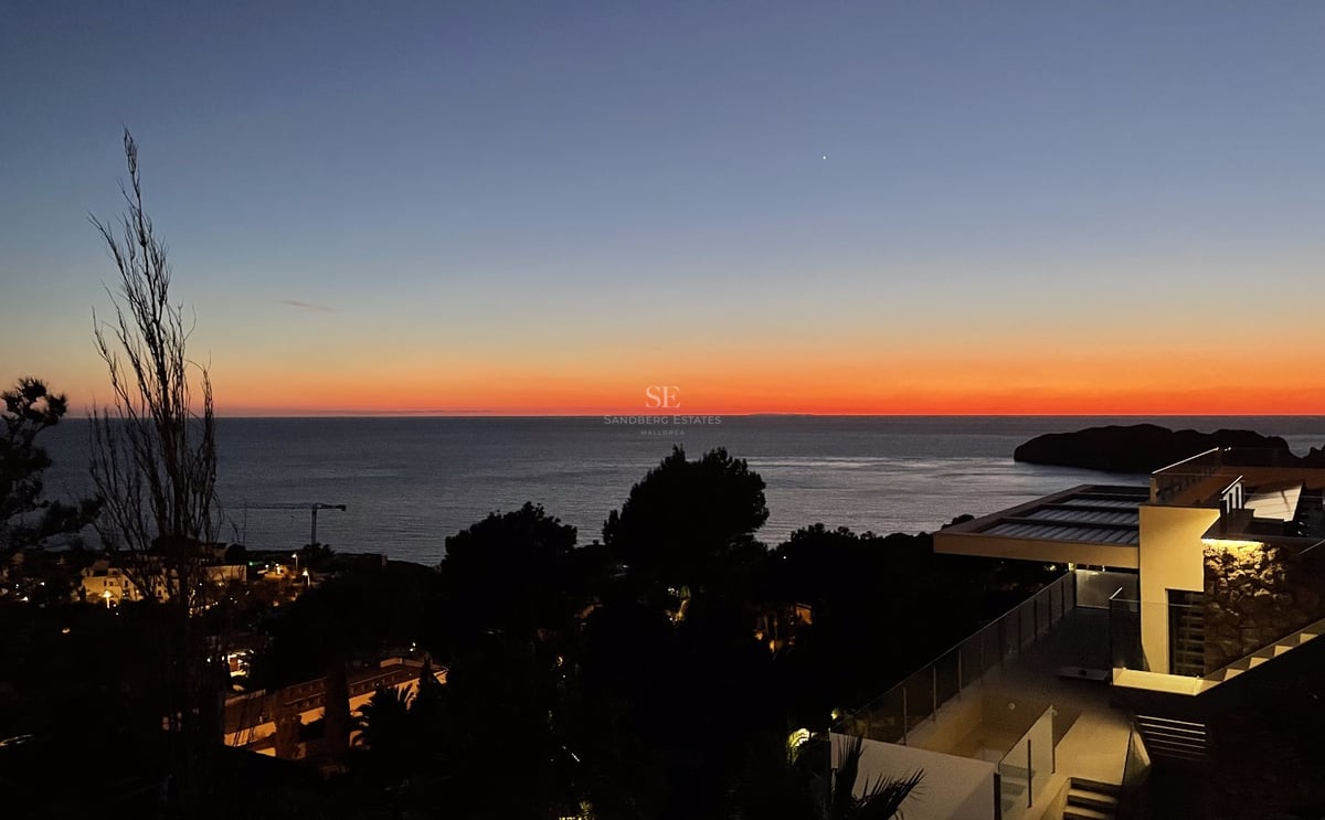Coucher de soleil sur la mer depuis la terrasse d'une villa moderne avec balustrades en verre et éclairage nocturne.