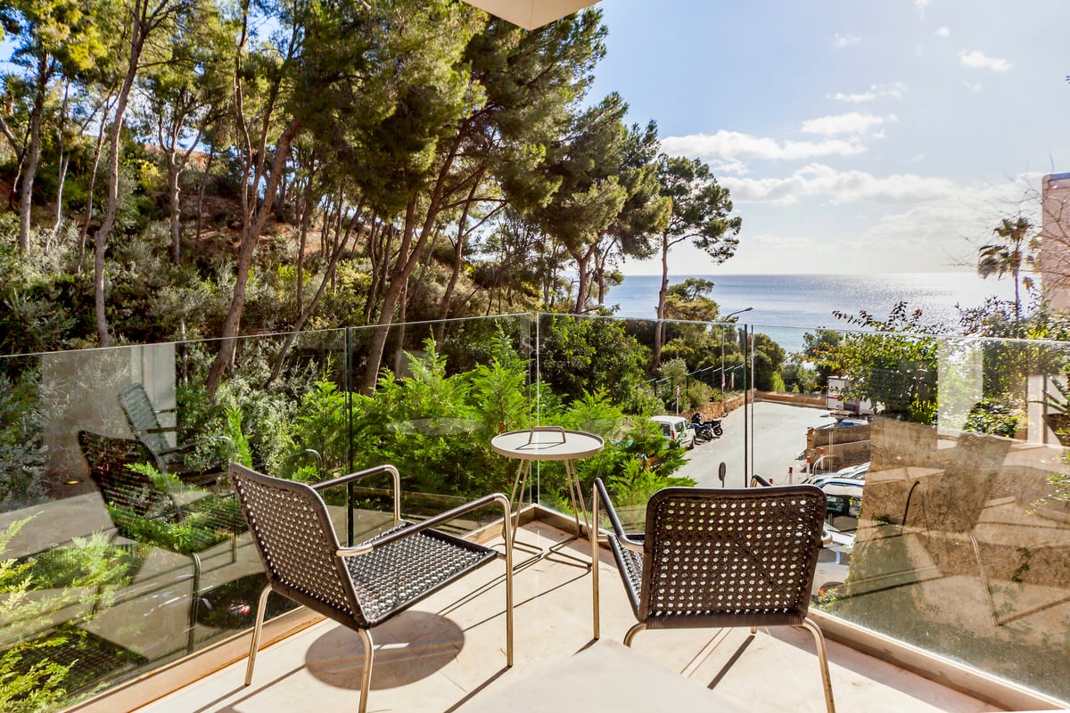 Terrasse avec garde-corps en verre et mobilier moderne donnant sur une pinède et la mer Méditerranée.