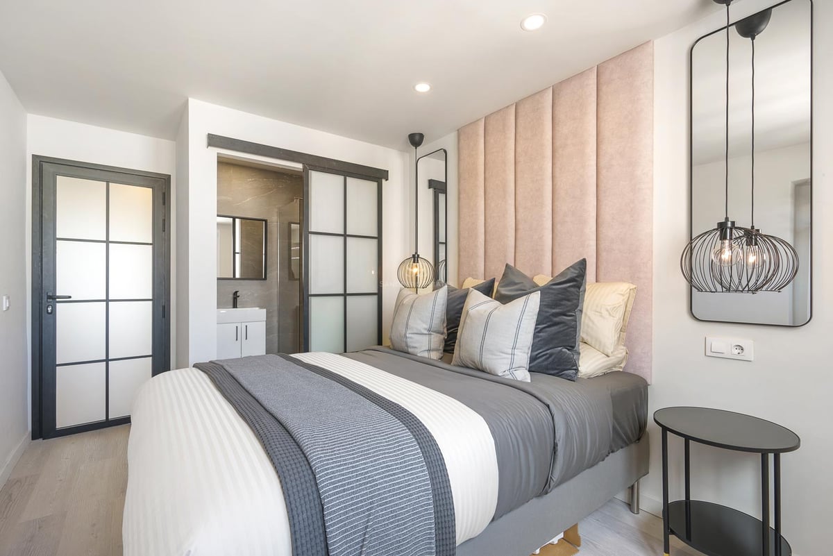 Chambre contemporaine avec tête de lit en velours rose, portes vitrées industrielles et salle d'eau attenante.