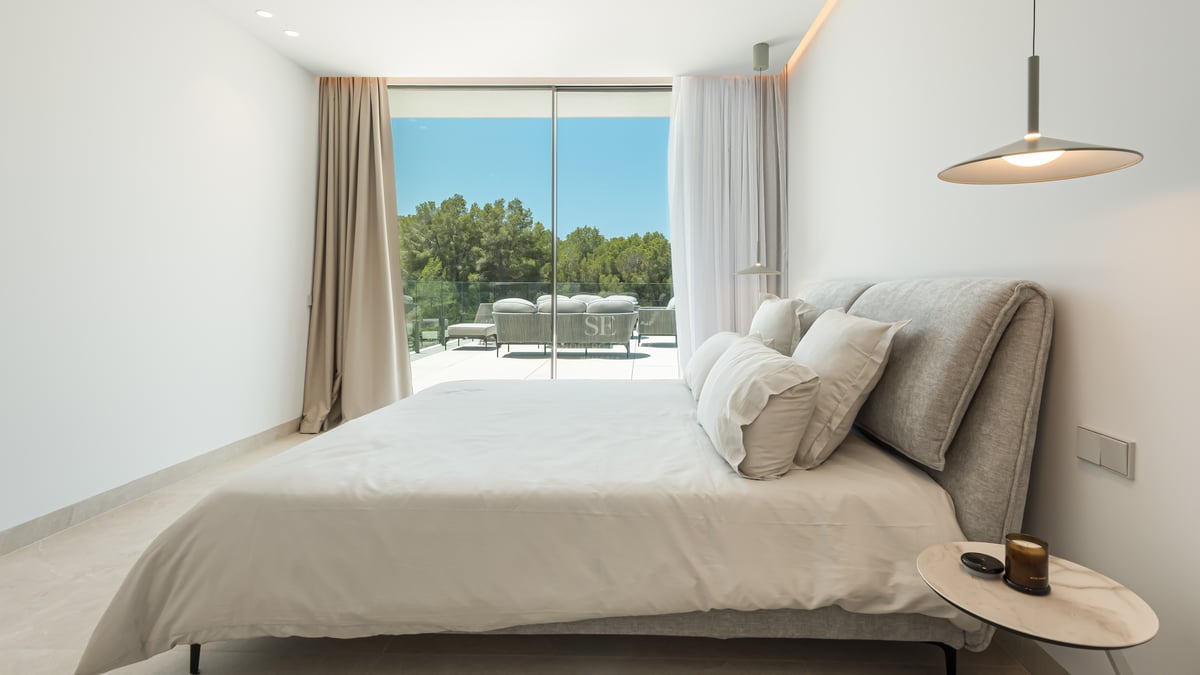 Chambre contemporaine avec grandes baies vitrées ouvrant sur une terrasse avec mobilier et vue sur les arbres.