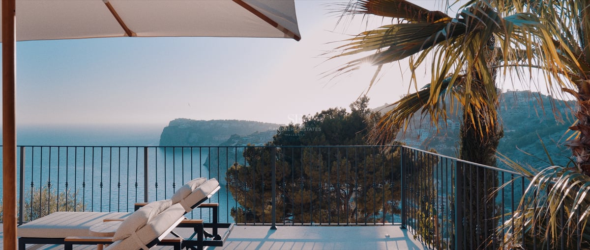 Bains de soleil sur une terrasse moderne surplombant une baie côtière avec des falaises et une mer bleue.