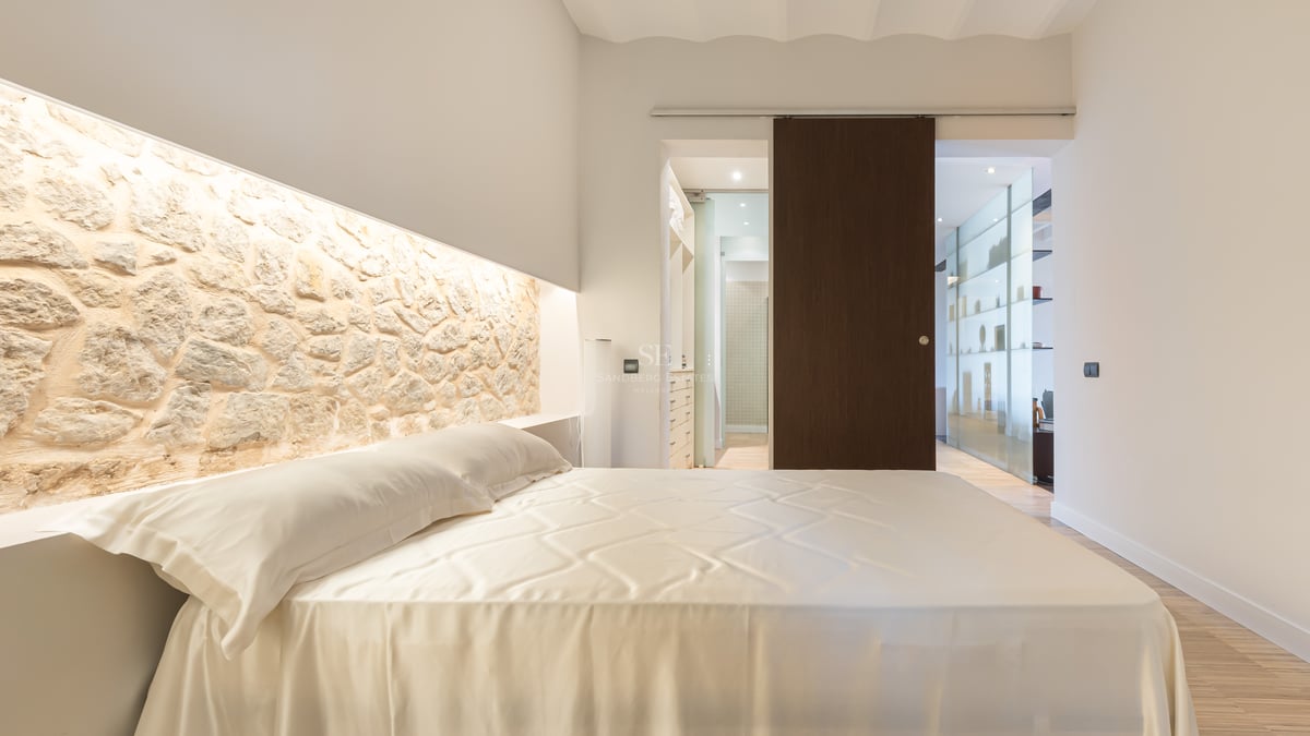 Chambre de luxe avec un grand lit, une tête de lit en pierre naturelle éclairée et une porte coulissante en bois sombre.