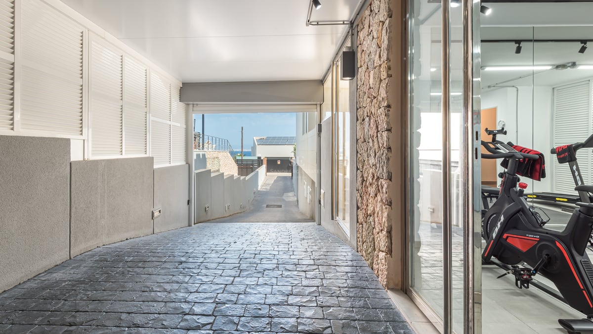 Allée pavée avec mur en pierre naturelle et vue sur une salle de sport privée à travers une paroi vitrée.