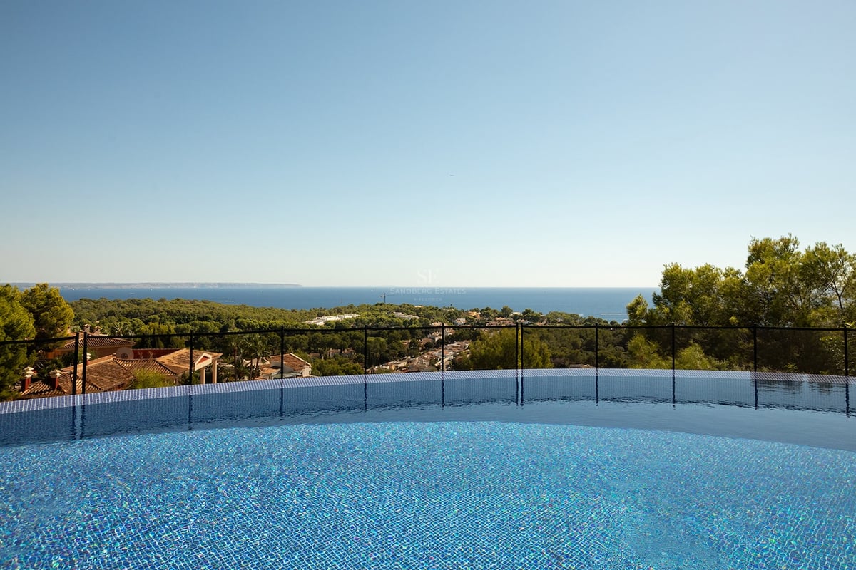 Vue depuis une piscine en mosaïque bleue surplombant la mer Méditerranée et un paysage verdoyant.