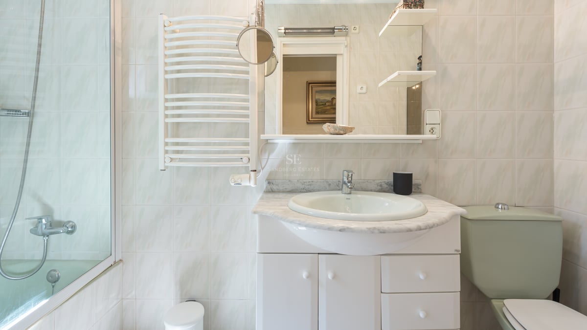Salle de bains avec meuble blanc, plan en marbre gris, miroir, sèche-serviettes et carrelage mural clair.