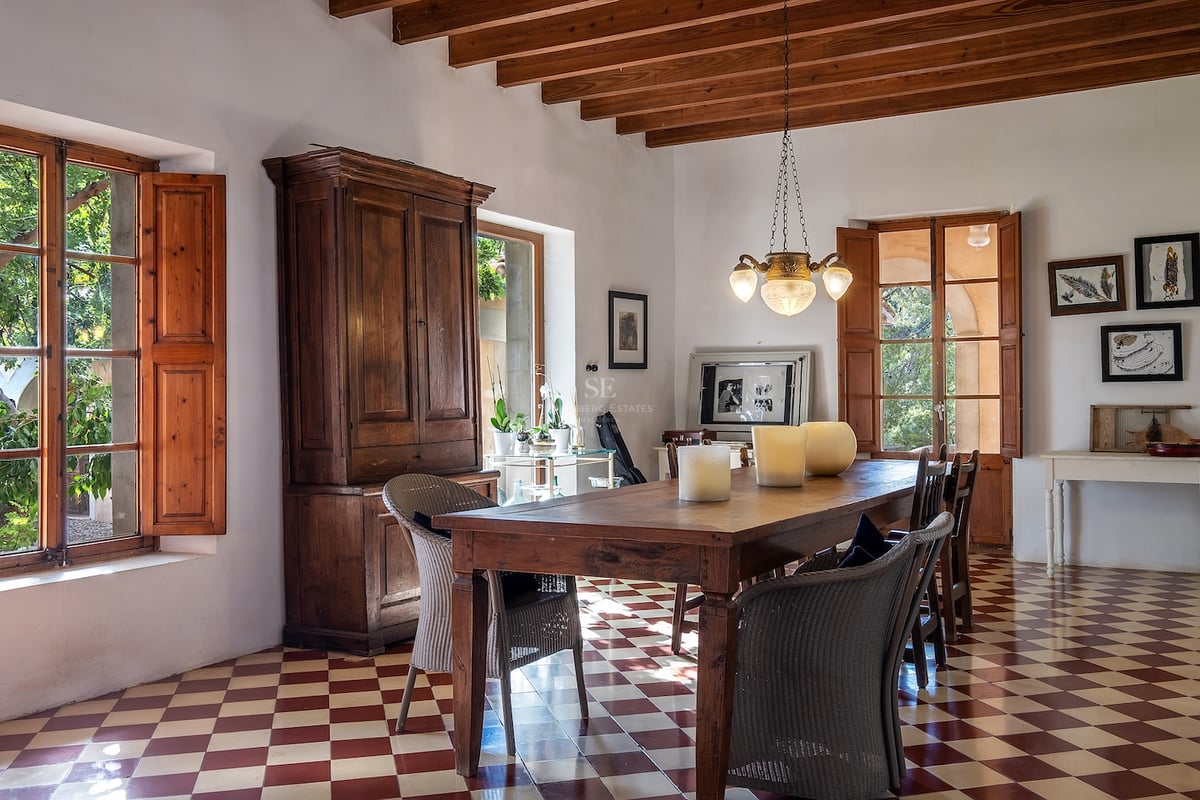 Salle à manger rustique avec table en bois, sol en damier rouge et blanc et poutres apparentes.