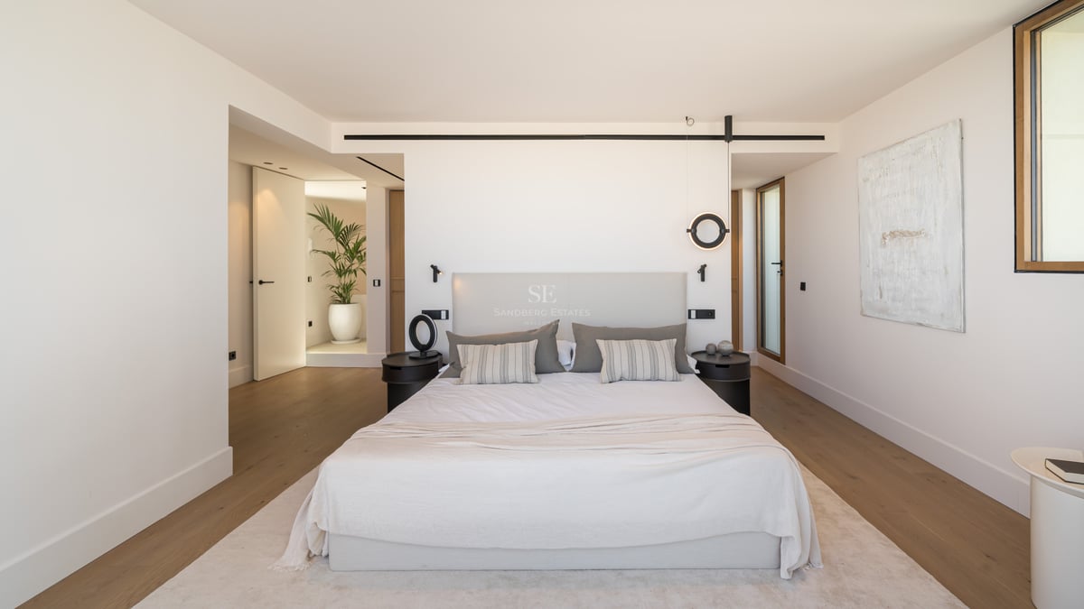 Chambre de maître minimaliste avec grand lit, linge de lit neutre, parquet en chêne et luminaires design noirs.