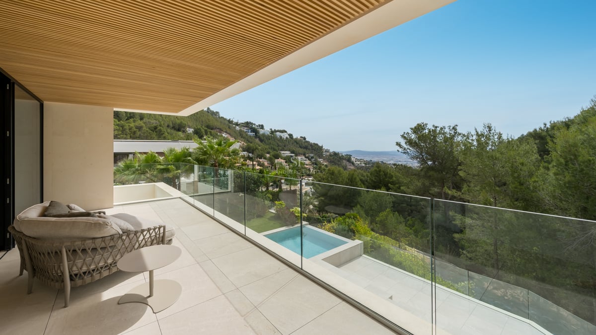 Terrasse moderne avec garde-corps en verre, sol en pierre et plafond en bois, offrant une vue sur la colline et la piscine.