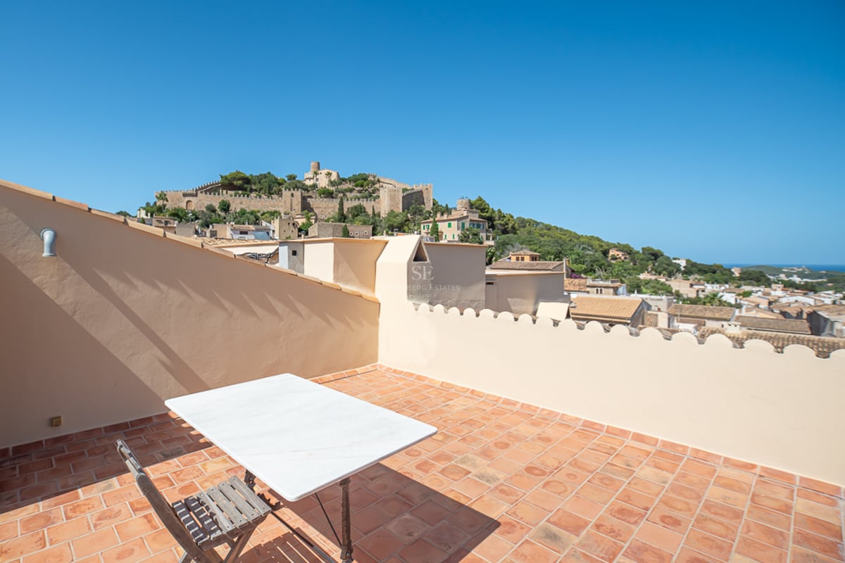 Rooftop terrace with terracotta tiles and marble table, overlooking a historic castle on a lush green hill.