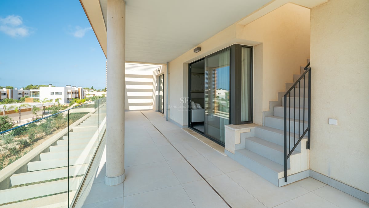 Amplia terraza soleada con baldosas de gran formato, barandilla de cristal y escalera exterior en una villa moderna.