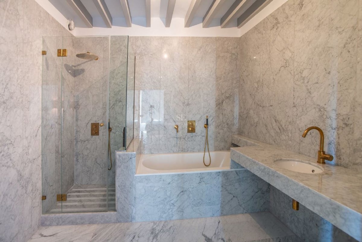 Baño de lujo con paredes de mármol, ducha de cristal, bañera integrada y elegantes grifos de latón.