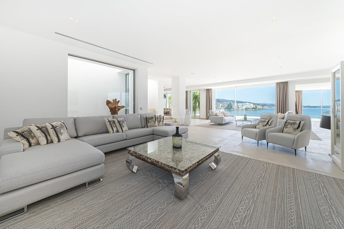 Grand salon moderne avec canapés gris clair, table basse en verre et grandes baies vitrées donnant sur la mer.