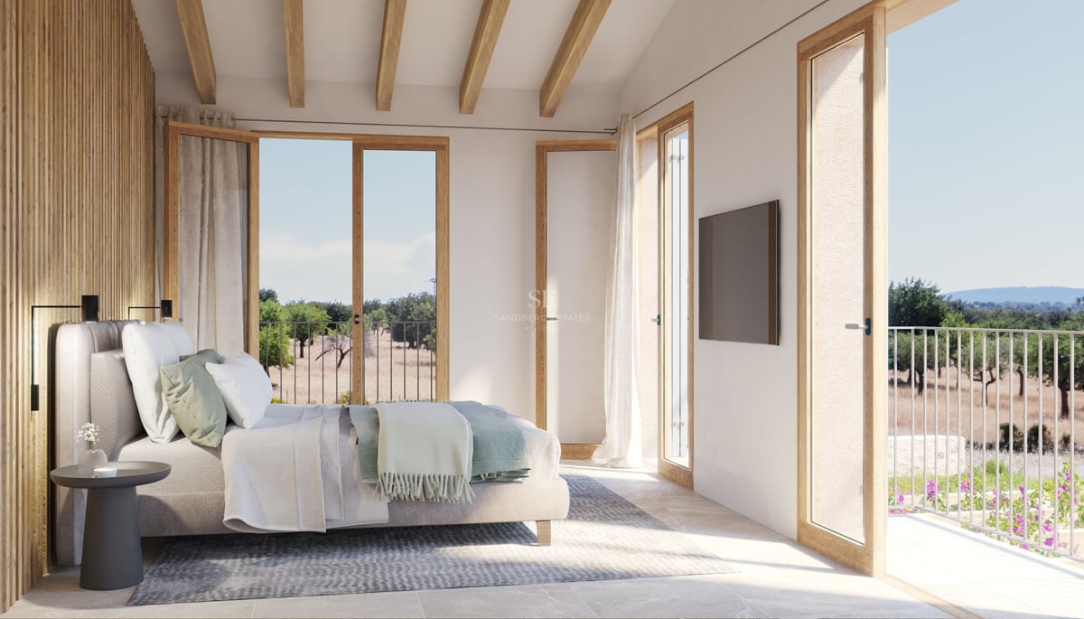 Chambre principale lumineuse avec poutres en bois, sol en pierre et portes-fenêtres ouvrant sur la nature.