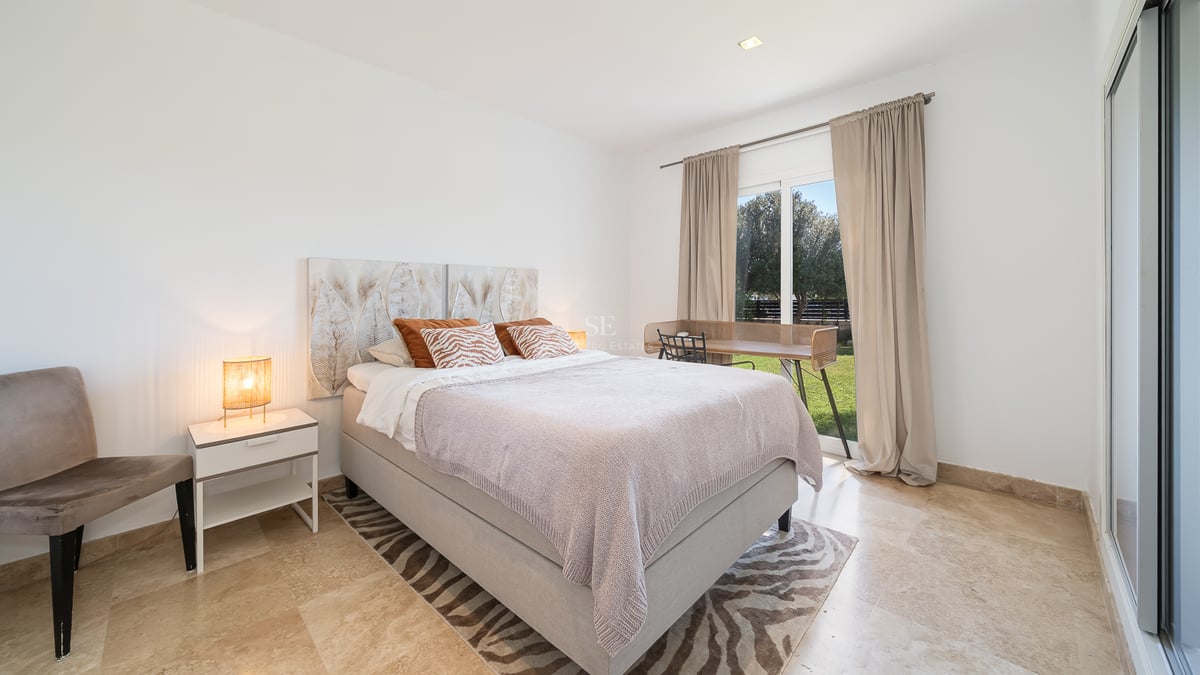 Chambre moderne avec sol en marbre, lit double et porte vitrée ouvrant sur un jardin verdoyant.
