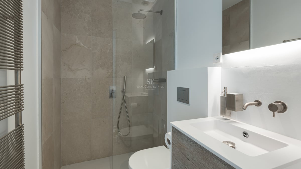 Salle de bains contemporaine avec carrelage en pierre, douche vitrée, meuble vasque suspendu et sèche-serviettes.