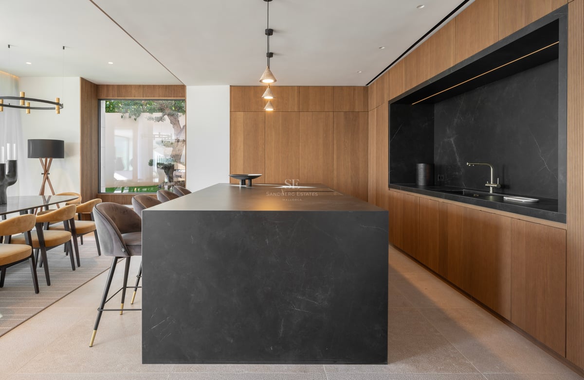Cuisine moderne avec un grand îlot en pierre noire, des meubles en chêne cannelé et des luminaires suspendus.