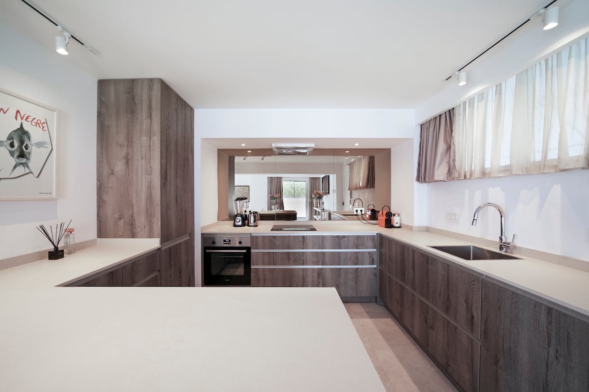 Cuisine minimaliste avec placards en bois sombre, plans de travail blancs et éclairage sur rails.