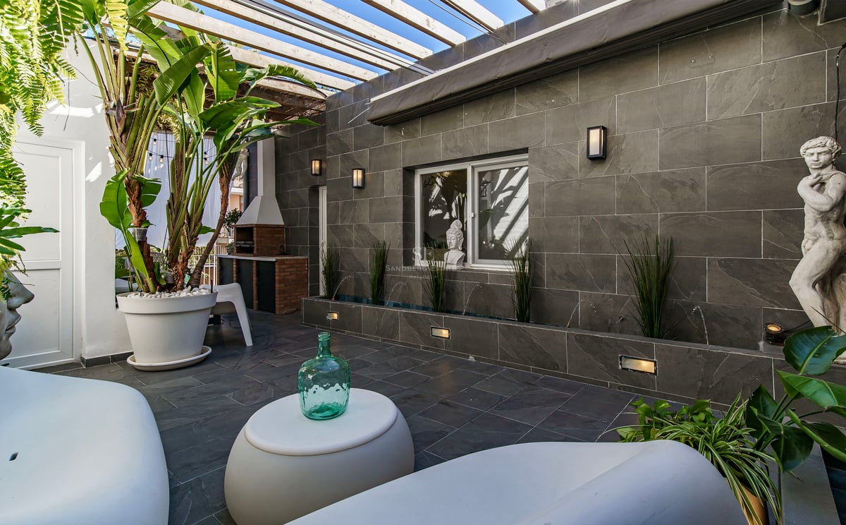Patio de luxe avec murs en pierre grise, mobilier moderne blanc, pergola en bois et plantes tropicales.