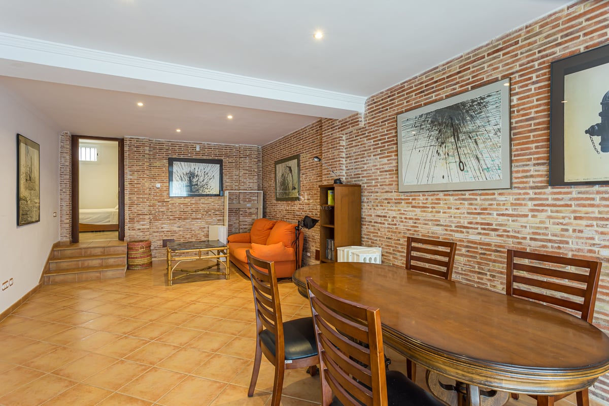 Salle à manger avec table en bois et canapé orange devant un mur en briques apparentes dans un intérieur chaleureux.