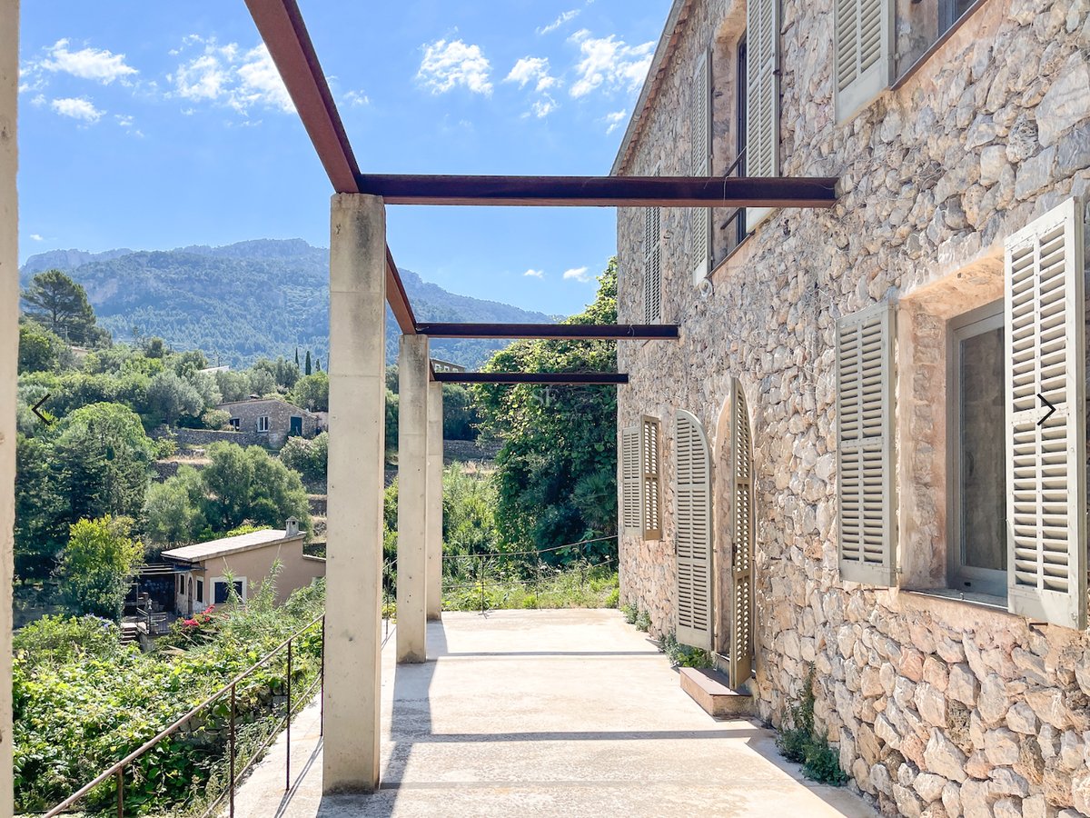 Façade en pierre naturelle d'une villa méditerranéenne avec terrasse surélevée donnant sur une vallée montagneuse.