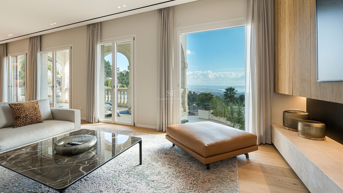 Salon moderne avec table en marbre, pouf en cuir et baies vitrées offrant une vue sur la mer Méditerranée.