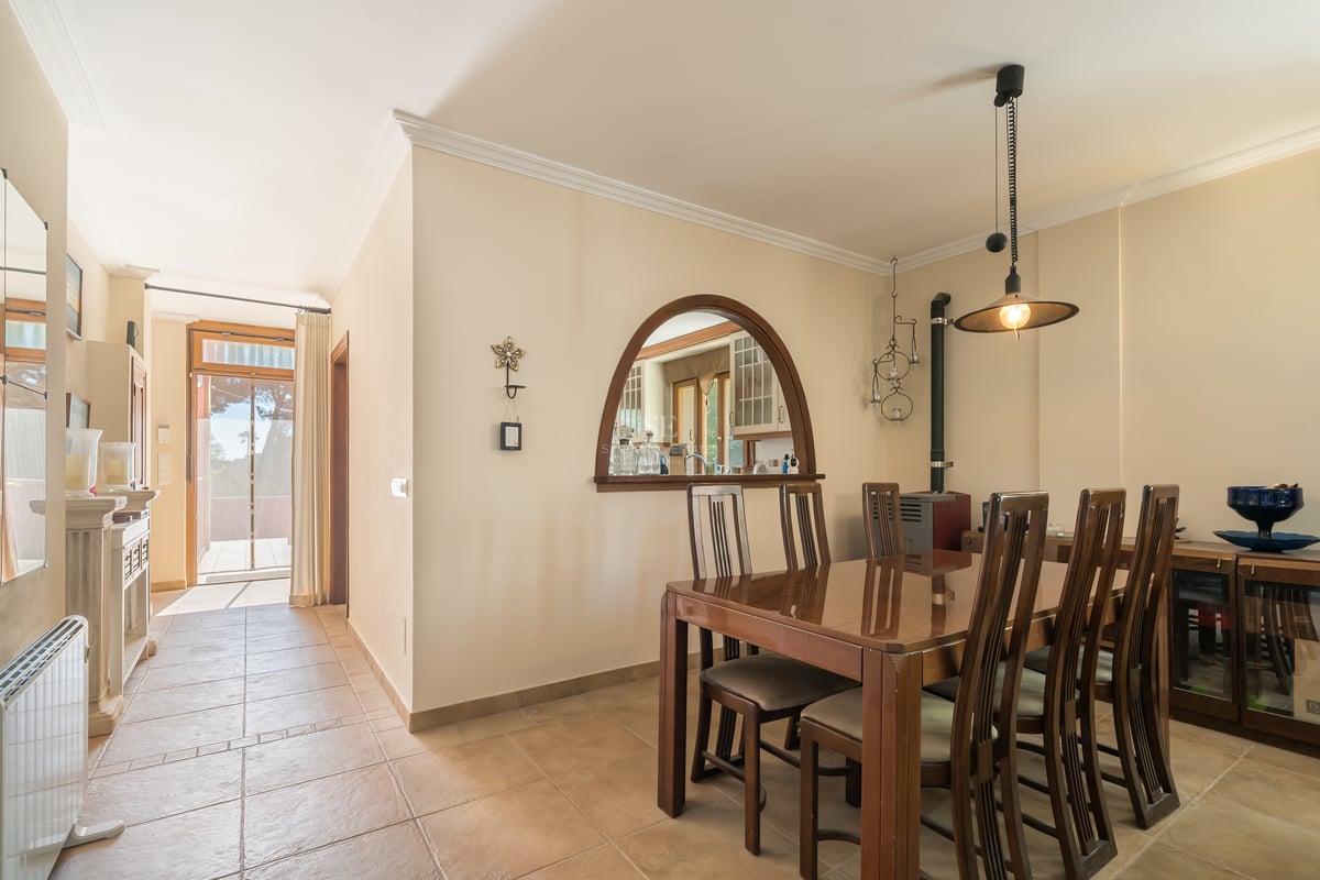 Salle à manger avec table en bois sombre, sol en terre cuite et arche ouvrant sur la cuisine dans une villa.