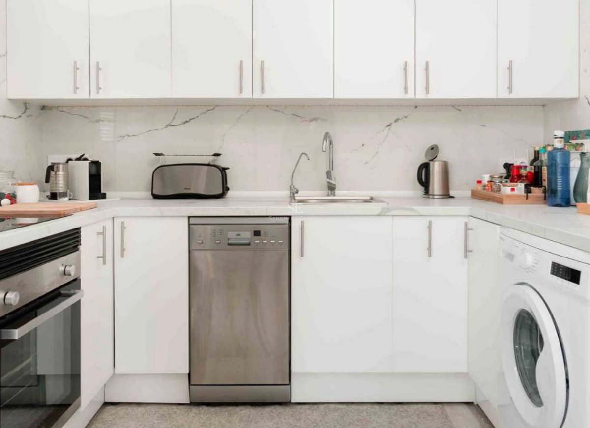 Cuisine blanche moderne avec plan de travail en marbre, lave-vaisselle en inox et rangements épurés.