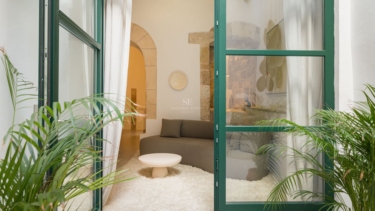 Vue à travers des portes vitrées vertes sur un salon avec canapé incurvé, tapis blanc et arches en pierre.