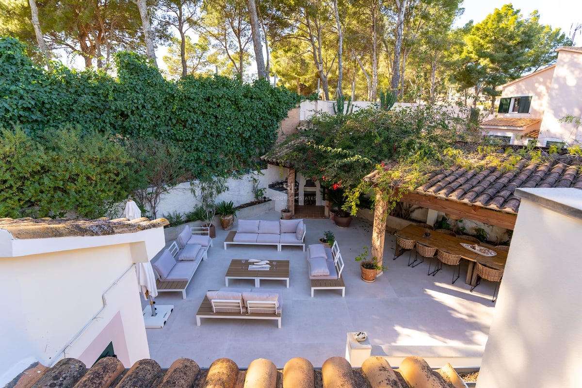 Vue surélevée d'une spacieuse terrasse pavée avec des canapés blancs, une grande table à manger en bois et des murs végétalisés.
