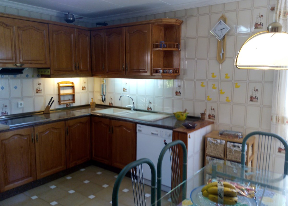Cuisine en L avec des meubles en chêne miel, du carrelage mural décoratif et un coin repas.