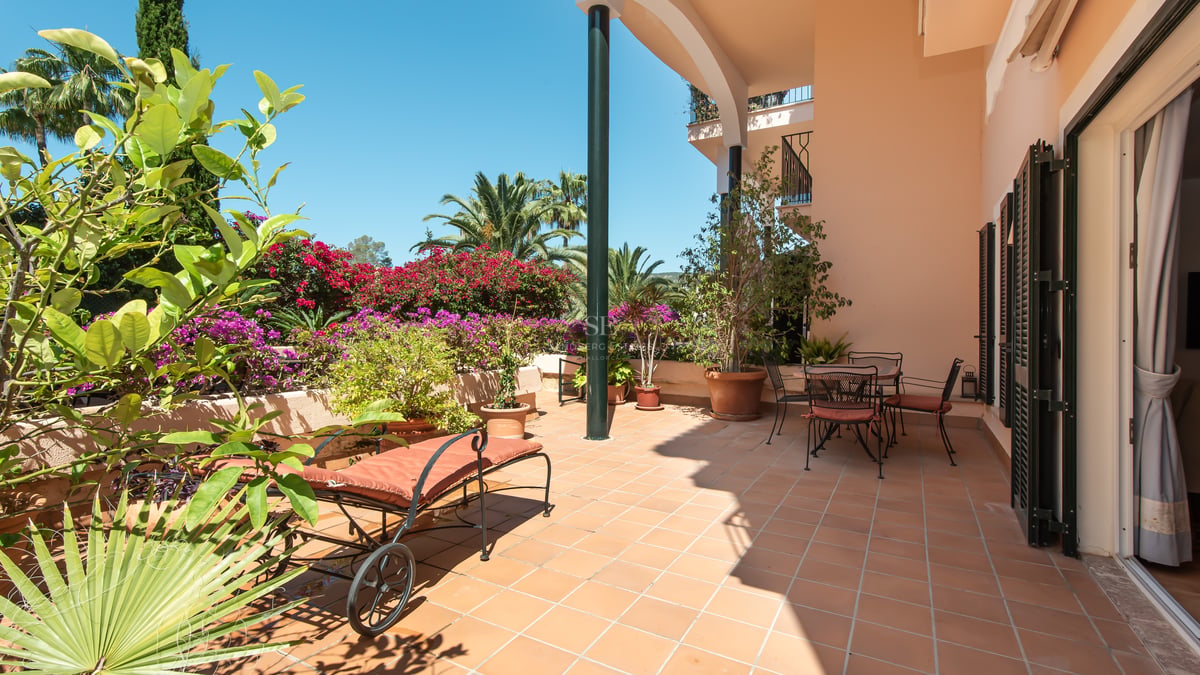 Terrasse en terre cuite avec chaise longue et coin repas, entourée de bougainvilliers et de palmiers sous un ciel bleu.