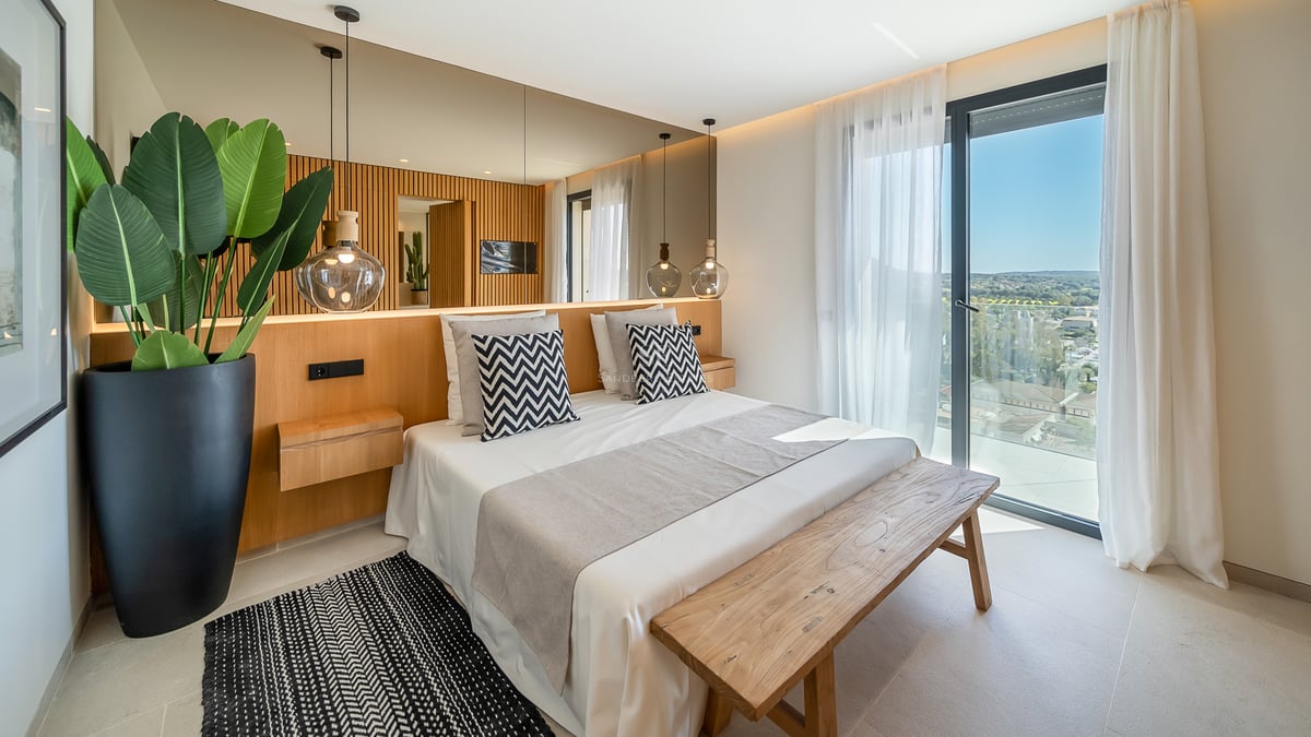 Chambre lumineuse avec tête de lit en bois, grand miroir, suspensions en verre et accès au balcon.