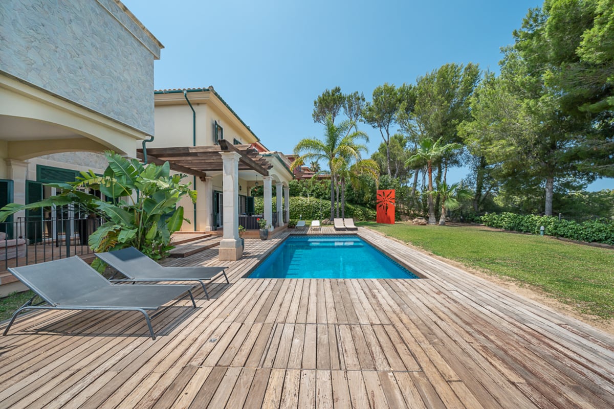 Piscine extérieure rectangulaire entourée d'un deck en bois, transats et jardin méditerranéen luxuriant.