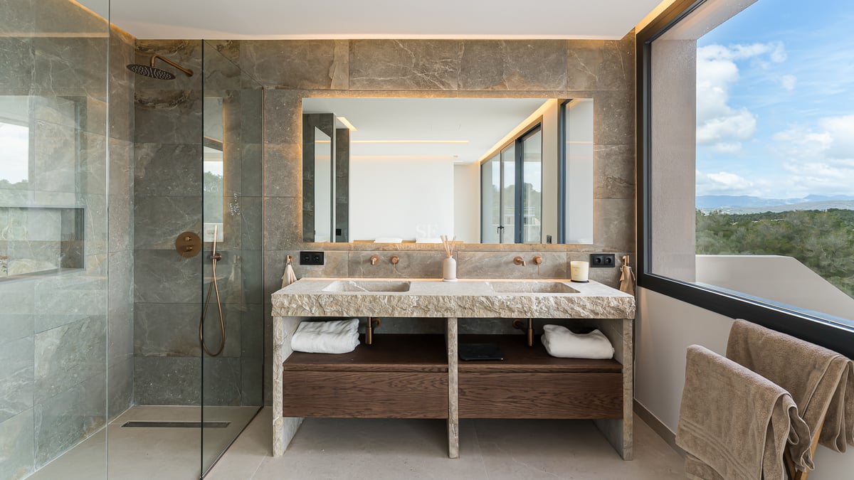 Salle de bains de luxe avec double vasque en pierre naturelle, grand miroir rétroéclairé et finitions en bois sombre.