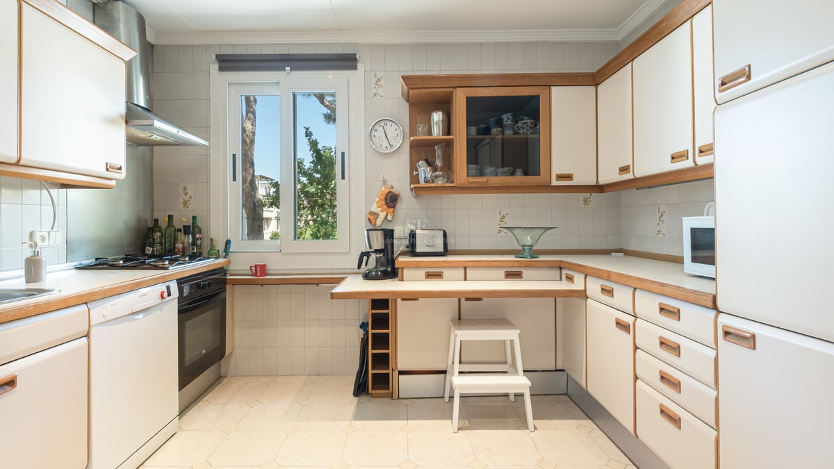 Cuisine claire avec placards blancs, finitions en bois, plan de travail fonctionnel et fenêtre sur le jardin.