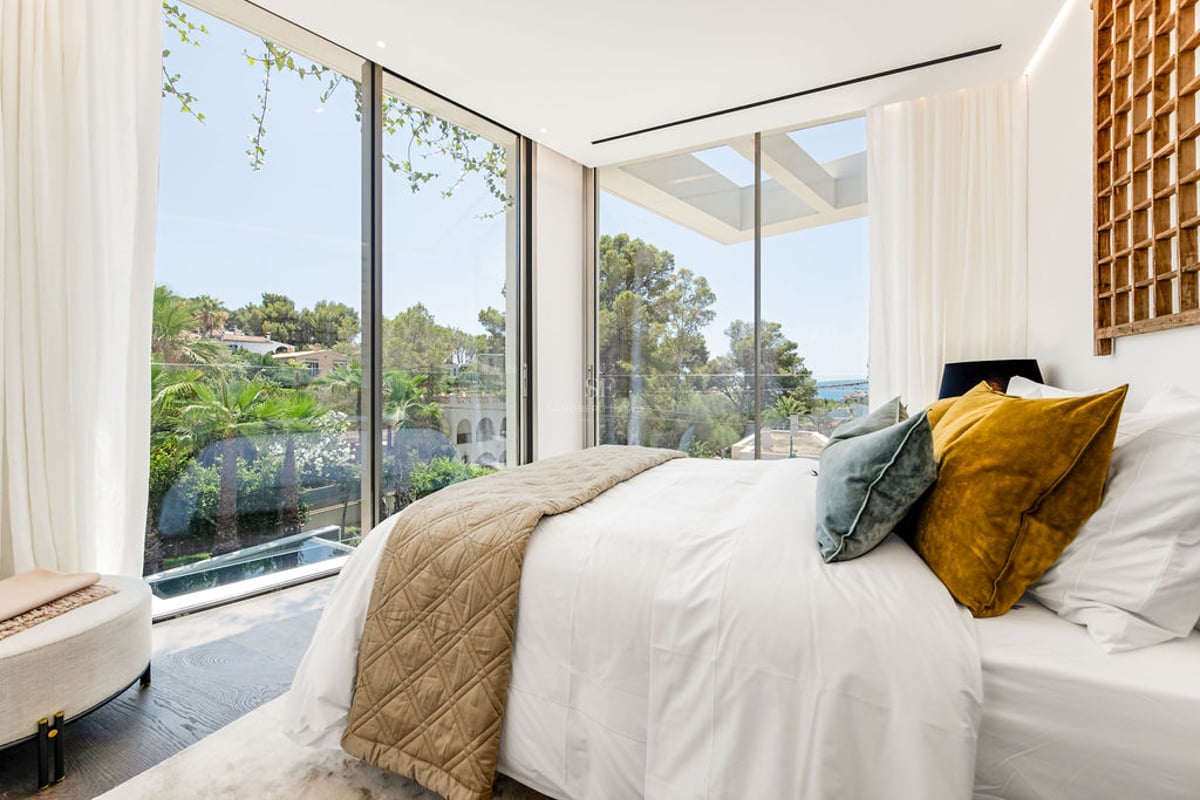 Chambre principale contemporaine avec de grandes baies vitrées donnant sur des palmiers et de la verdure.