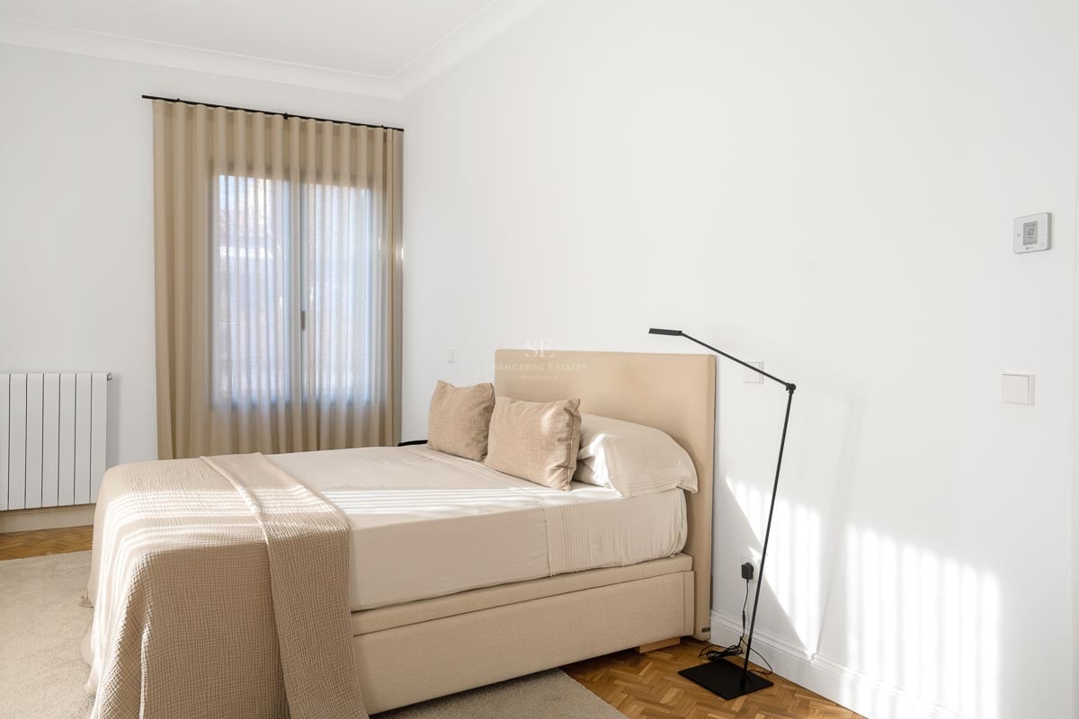Chambre lumineuse avec un lit beige, des murs blancs et un parquet en bois chaleureux.