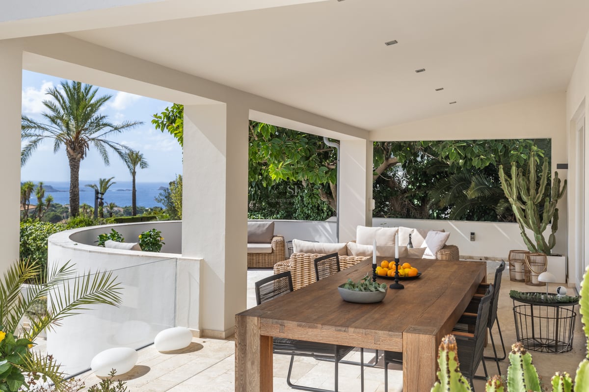 Terrasse couverte avec grande table en bois, canapés en rotin et vue sur la mer Méditerranée et les palmiers.