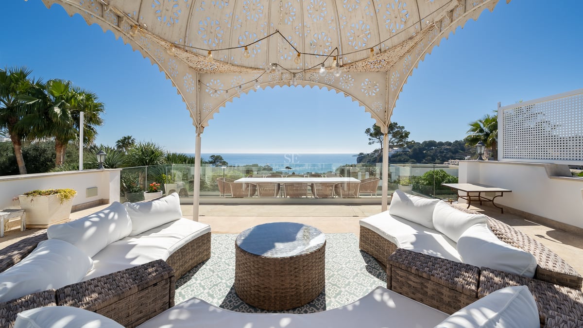Grande terrasse avec canapés en osier sous un pavillon décoratif offrant une vue imprenable sur l'océan.