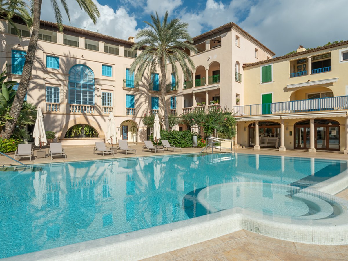 Vue grand angle d'une piscine turquoise avec chaises longues et architecture méditerranéenne traditionnelle en arrière-plan.