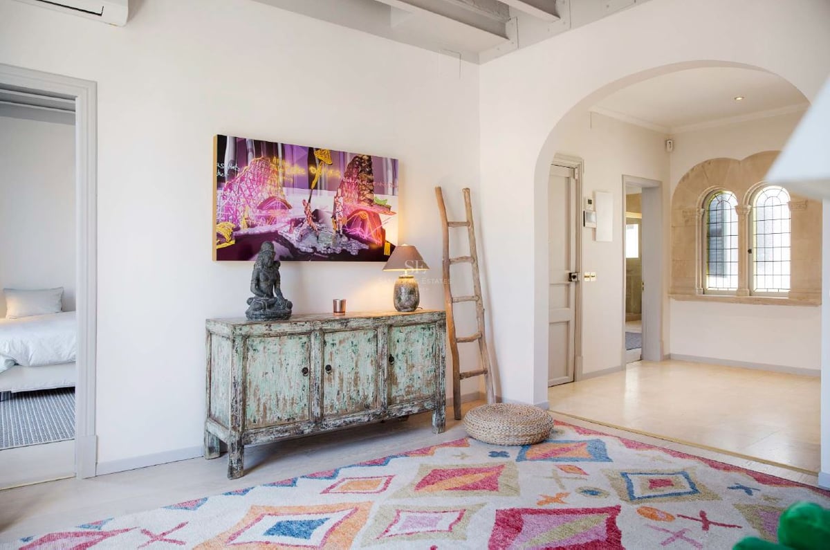 Pasillo interior con alfombra geométrica, aparador turquesa vintage, escalera rústica y ventanas de piedra en arco.