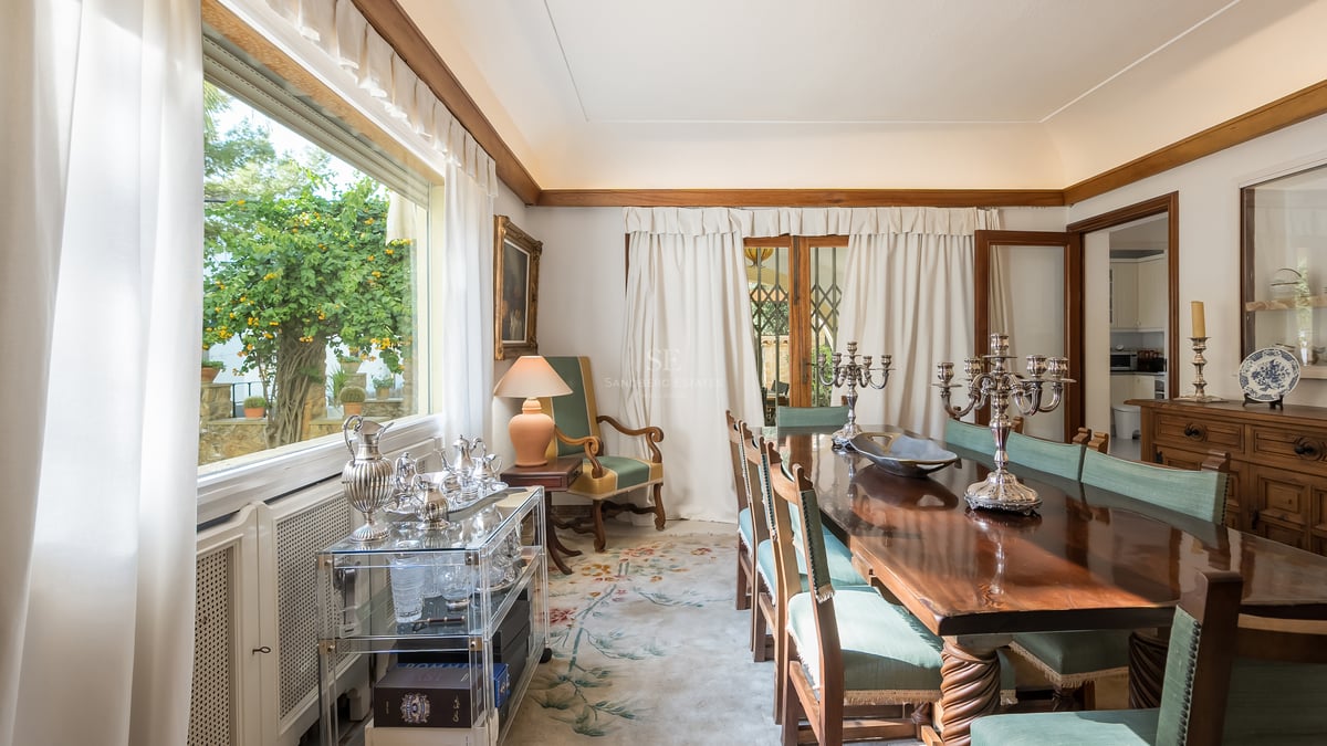 Salle à manger formelle avec table en bois poli, chaises vertes et candélabres en argent devant une grande fenêtre.