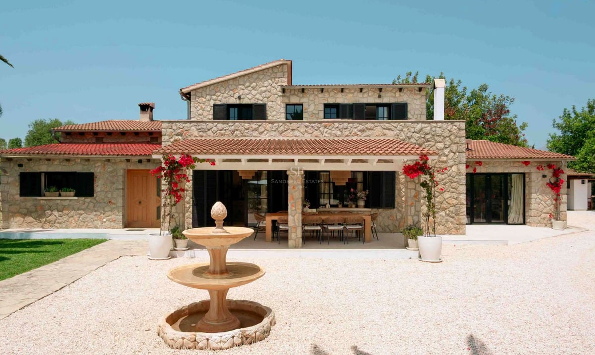 Extérieur d'une villa en pierre avec toit en terre cuite, porche couvert avec salle à manger et fontaine.