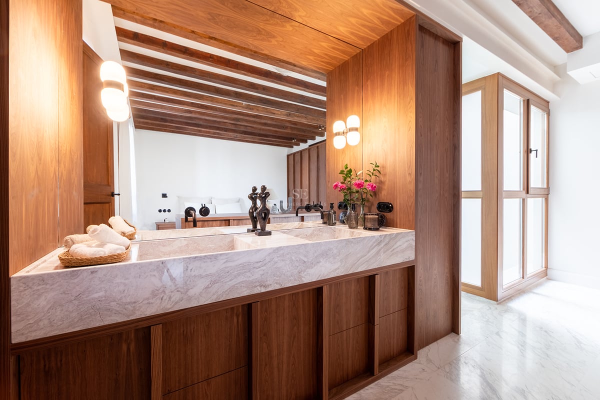 Baño principal moderno con lavabo doble de mármol, muebles de nogal y vigas de madera vistas.